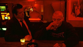 Movie still from “Pusher II” (2004), directed by Nicolas Winding Refn – Two men are sitting at a table and one is drinking; Medium shot, Over the shoulder angle