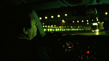 Movie still from “Pusher II” (2004), directed by Nicolas Winding Refn – A man sitting in the drivers seat of a car at night; Medium shot, Over the shoulder angle