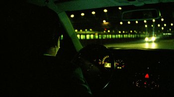 Movie still from “Pusher II” (2004), directed by Nicolas Winding Refn – A man sitting in the drivers seat of a car at night; Medium shot, Over the shoulder angle