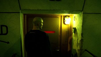 Movie still from “Pusher II” (2004), directed by Nicolas Winding Refn – A man standing in front of an open door in a room; Medium shot, High angle