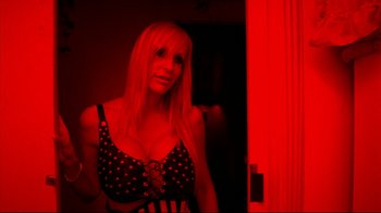Movie still from “Pusher II” (2004), directed by Nicolas Winding Refn – A woman standing in front of a door in a red room; Medium shot, Low angle
