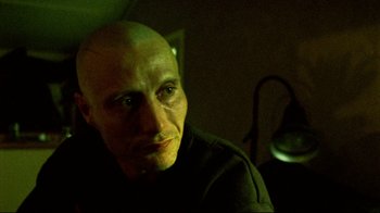 Movie still from “Pusher II” (2004), directed by Nicolas Winding Refn – A man with bald head sitting in a dark room; Close Up shot, Low angle