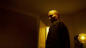 Movie still from “Pusher II” (2004), directed by Nicolas Winding Refn – A man standing in a dark room with his head turned to the side; Medium shot, Low angle