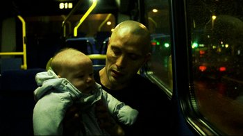 Movie still from “Pusher II” (2004), directed by Nicolas Winding Refn – A man holding a baby on a bus; Close Up shot, Over the shoulder angle