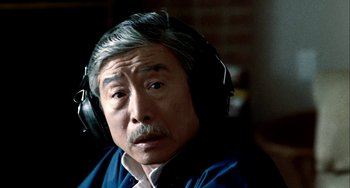 Movie still from “Pushing Hands” (1991), directed by Ang Lee – An older man wearing a pair of headphones; Close Up shot, Over the shoulder angle