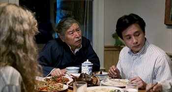 Movie still from “Pushing Hands” (1991), directed by Ang Lee – Two people sitting at a dinner table with plates of food on the table; Medium shot, Over the shoulder angle