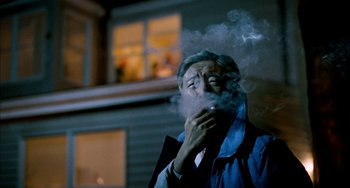 Movie still from “Pushing Hands” (1991), directed by Ang Lee – An older man smoking a cigarette in front of a building; Medium shot, Low angle
