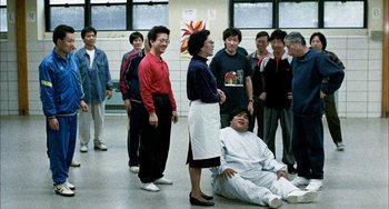 Movie still from “Pushing Hands” (1991), directed by Ang Lee – A group of people standing around a man in a room; Wide shot, High angle
