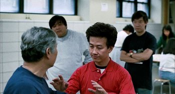 Movie still from “Pushing Hands” (1991), directed by Ang Lee – A group of people in a room talking to each other; Medium shot, Over the shoulder angle