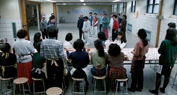 Movie still from “Pushing Hands” (1991), directed by Ang Lee – A group of people standing around a room with chairs; Wide shot, High angle
