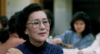 Movie still from “Pushing Hands” (1991), directed by Ang Lee – An older woman wearing glasses looking at the camera; Close Up shot, Over the shoulder angle
