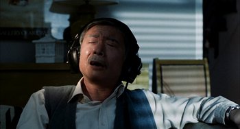 Movie still from “Pushing Hands” (1991), directed by Ang Lee – An older man wearing headphones while sitting in a chair; Close Up shot, High angle
