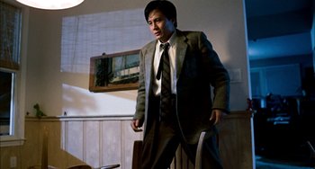 Movie still from “Pushing Hands” (1991), directed by Ang Lee – A man in a suit and tie standing in a room; Medium shot, Low angle