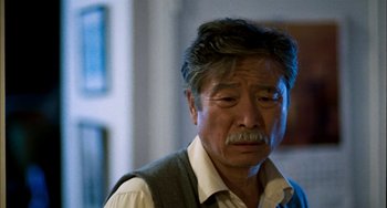 Movie still from “Pushing Hands” (1991), directed by Ang Lee – An older asian man with a beard and mustache; Close Up shot, Over the shoulder angle