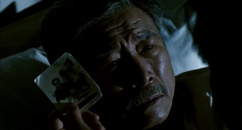 Movie still from “Pushing Hands” (1991), directed by Ang Lee – An older man is holding a photo of himself in the dark; Close Up shot, High angle