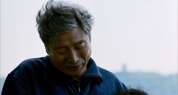 Movie still from “Pushing Hands” (1991), directed by Ang Lee – An older man with grey hair is smiling; Close Up shot, Over the shoulder angle