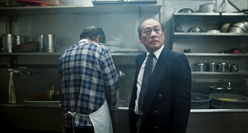 Movie still from “Pushing Hands” (1991), directed by Ang Lee – A man in a suit standing next to another man in an apron in a kitchen; Medium shot, Low angle