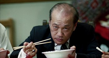 Movie still from “Pushing Hands” (1991), directed by Ang Lee – An older man in a business suit eats a bowl of rice with chopsticks; Close Up shot, Low angle