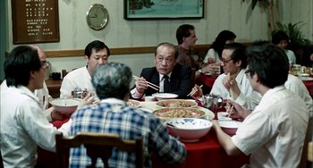 Movie still from “Pushing Hands” (1991), directed by Ang Lee – A group of people sitting around a table eating pizza; Medium shot, Over the shoulder angle