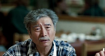 Movie still from “Pushing Hands” (1991), directed by Ang Lee – An older man wearing an apron looking at the camera; Close Up shot, Over the shoulder angle