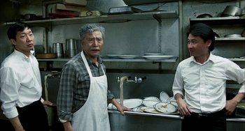 Movie still from “Pushing Hands” (1991), directed by Ang Lee – A man in a kitchen with an apron on; Medium shot, High angle