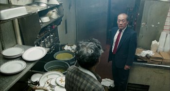 Movie still from “Pushing Hands” (1991), directed by Ang Lee – A man in a suit standing in front of a table; Medium shot, High angle