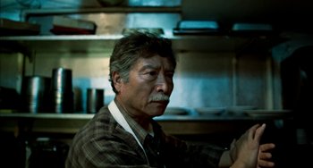 Movie still from “Pushing Hands” (1991), directed by Ang Lee – An older man sitting in front of a counter; Close Up shot, Low angle