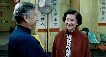Movie still from “Pushing Hands” (1991), directed by Ang Lee – An older man and a younger woman smiling at each other in front of a fan; Medium shot, Over the shoulder angle