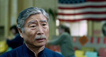 Movie still from “Pushing Hands” (1991), directed by Ang Lee – An older man in a blue shirt is looking at the camera; Close Up shot, Over the shoulder angle