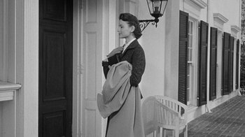 Movie still from “Queen Bee” (1955), directed by Ranald MacDougall – A black and white photo of a woman holding a coat; Wide shot, Over the shoulder angle