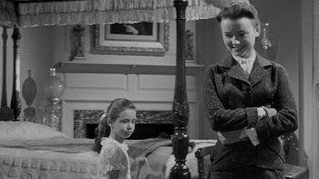 Movie still from “Queen Bee” (1955), directed by Ranald MacDougall – A woman standing next to a young girl in front of a fireplace; Medium shot, Over the shoulder angle