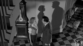 Movie still from “Queen Bee” (1955), directed by Ranald MacDougall – A man and a woman standing next to each other in front of a clock; Wide shot, Low angle