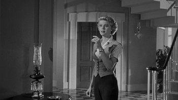 Movie still from “Queen Bee” (1955), directed by Ranald MacDougall – A black and white photo of a woman standing in front of a door; Medium shot, Low angle