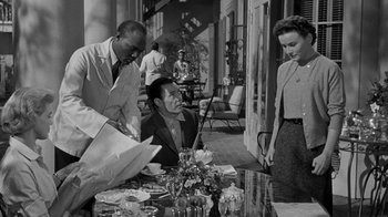 Movie still from “Queen Bee” (1955), directed by Ranald MacDougall – A group of people standing around a table; Medium shot, Over the shoulder angle