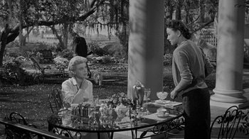 Movie still from “Queen Bee” (1955), directed by Ranald MacDougall – Two women sitting at a table in a garden; Wide shot, High angle