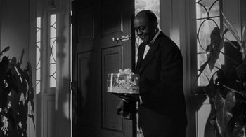 Movie still from “Queen Bee” (1955), directed by Ranald MacDougall – A black and white photo of a man in a suit holding a cake; Medium shot, Low angle