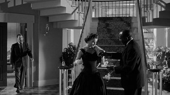 Movie still from “Queen Bee” (1955), directed by Ranald MacDougall – A man and a woman in formal wear standing in front of a staircase; Medium shot, Low angle