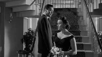 Movie still from “Queen Bee” (1955), directed by Ranald MacDougall – A man and a woman standing next to each other in front of a staircase; Medium shot, Low angle