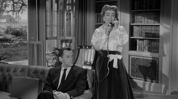 Movie still from “Queen Bee” (1955), directed by Ranald MacDougall – An older woman talking on a phone while a man sits on a couch; Medium shot, Low angle