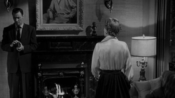 Movie still from “Queen Bee” (1955), directed by Ranald MacDougall – A woman standing in front of a fire place; Medium shot, Over the shoulder angle
