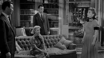 Movie still from “Queen Bee” (1955), directed by Ranald MacDougall – A man and a woman sitting on a couch in front of a book case; Wide shot, Over the shoulder angle