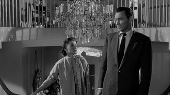 Movie still from “Queen Bee” (1955), directed by Ranald MacDougall – A man and a woman standing next to each other in front of chandeliers; Medium shot, Low angle