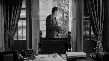 Movie still from “Queen Bee” (1955), directed by Ranald MacDougall – A black and white photo of a man standing in front of a window; Medium shot, Over the shoulder angle