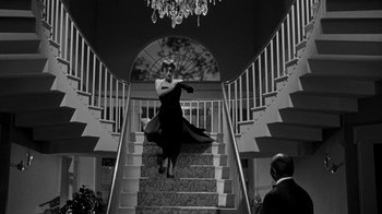 Movie still from “Queen Bee” (1955), directed by Ranald MacDougall – A woman in a black dress standing on a staircase; Wide shot, Low angle