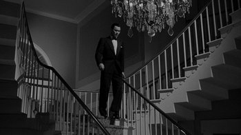 Movie still from “Queen Bee” (1955), directed by Ranald MacDougall – A black and white photo of a man in a tuxedo on a staircase; Wide shot, Low angle