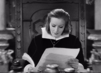 Movie still from “Queen Christina” (1933), directed by Rouben Mamoulian – A woman sitting at a table reading a piece of paper; Medium shot, High angle