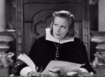 Movie still from “Queen Christina” (1933), directed by Rouben Mamoulian – A black and white photo of a woman sitting at a table; Medium shot, High angle