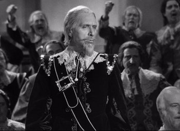 Movie still from “Queen Christina” (1933), directed by Rouben Mamoulian – An old man with a long beard wearing a suit and tie; Medium shot, Low angle