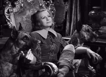 Movie still from “Queen Christina” (1933), directed by Rouben Mamoulian – A woman sitting in a chair with two dogs on her lap; Medium shot, High angle