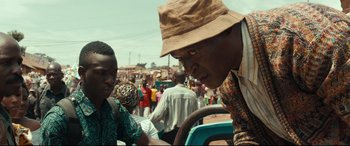 Movie still from “Queen of Katwe” (2016), directed by Mira Nair – A man wearing a hat is talking to another man in a car; Close Up shot, Over the shoulder angle